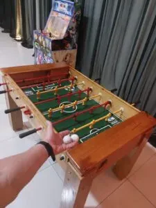 Foto de uma mesa de totó de madeira, com jogadores de plástico azuis e vermelhos, um clássico indispensável no aluguel de brinquedos para eventos.