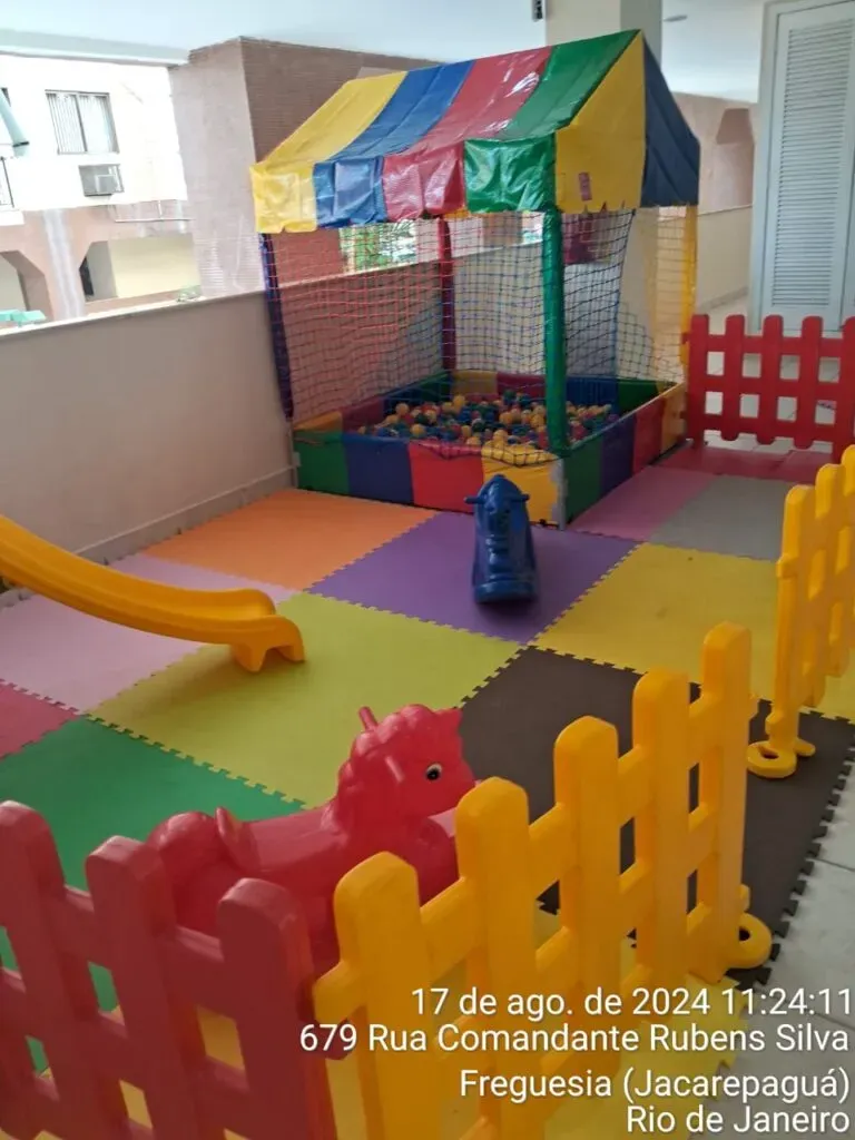 Foto de um kit área baby montado para locação, incluindo um escorregador colorido, piscina de bolinhas, gangorra, tapetes de EVA e cercado de grades."
