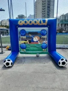 Foto de um chute a gol inflável com o design de uma trave de futebol e buracos com pontuações diferentes para testar a precisão, um item popular na locação de brinquedos infláveis.